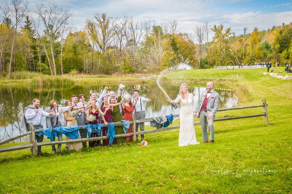 A wedding party cheering as the bride pops a bottle of champagne outside at Catamount Resort