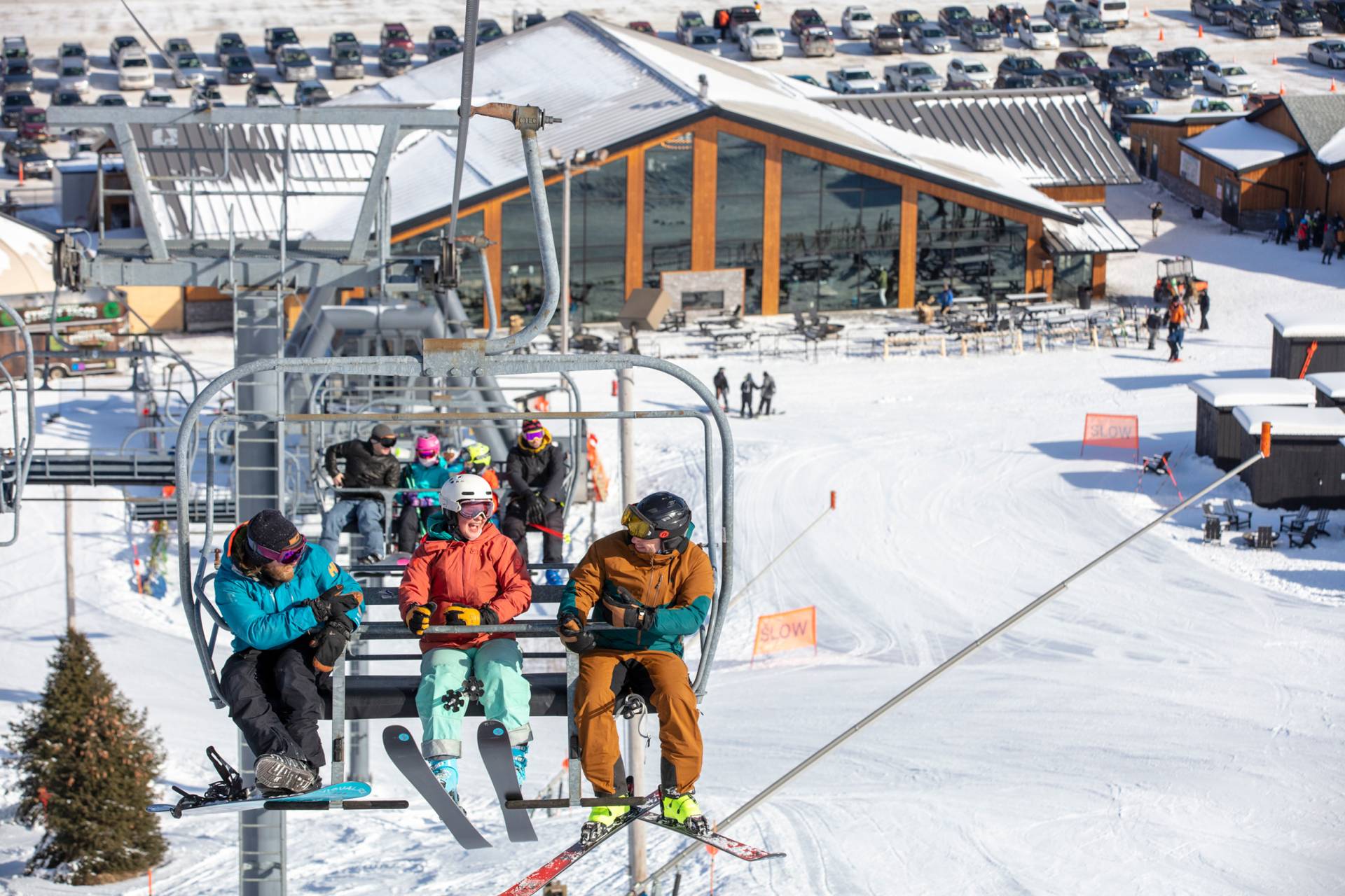 3 skiers riding on a chairlift with mountain lodge in background